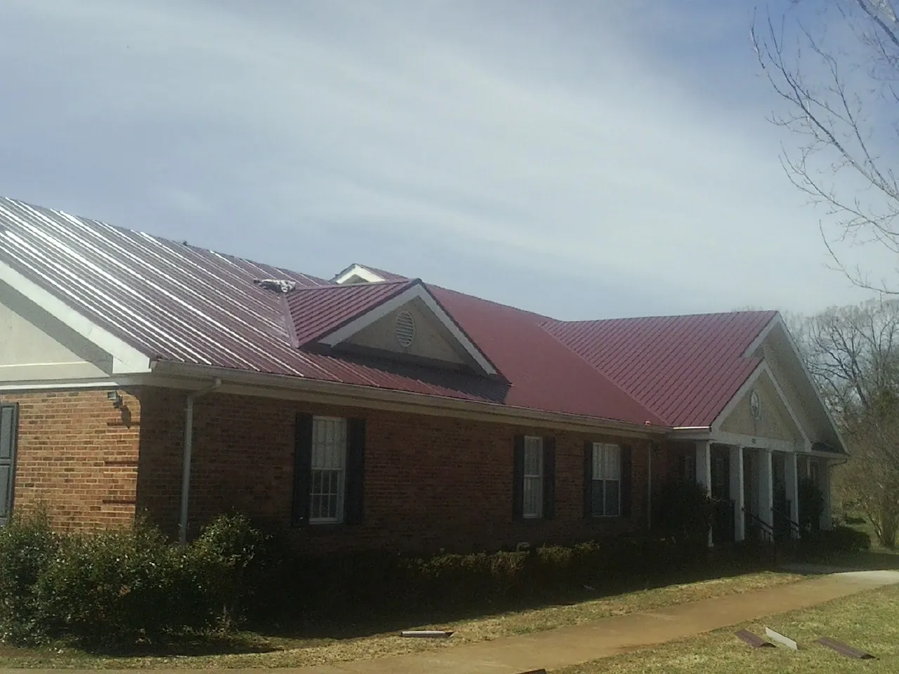 Red metal roof with gabled entries on a long brick building, from a Hail Damage Roof Repair job in Great Falls