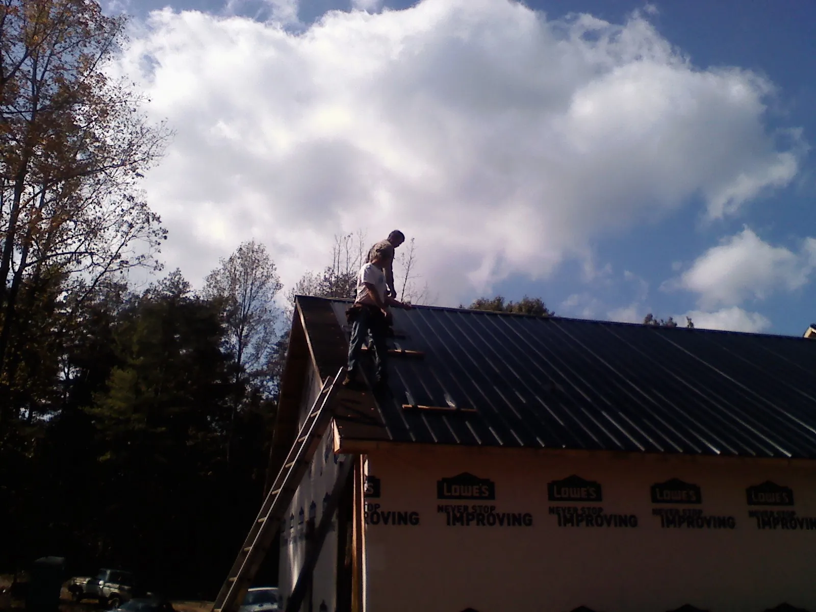 Roofer fastening dark metal panels high against a cloudy sky, from a Roof Inspection job in Great Falls