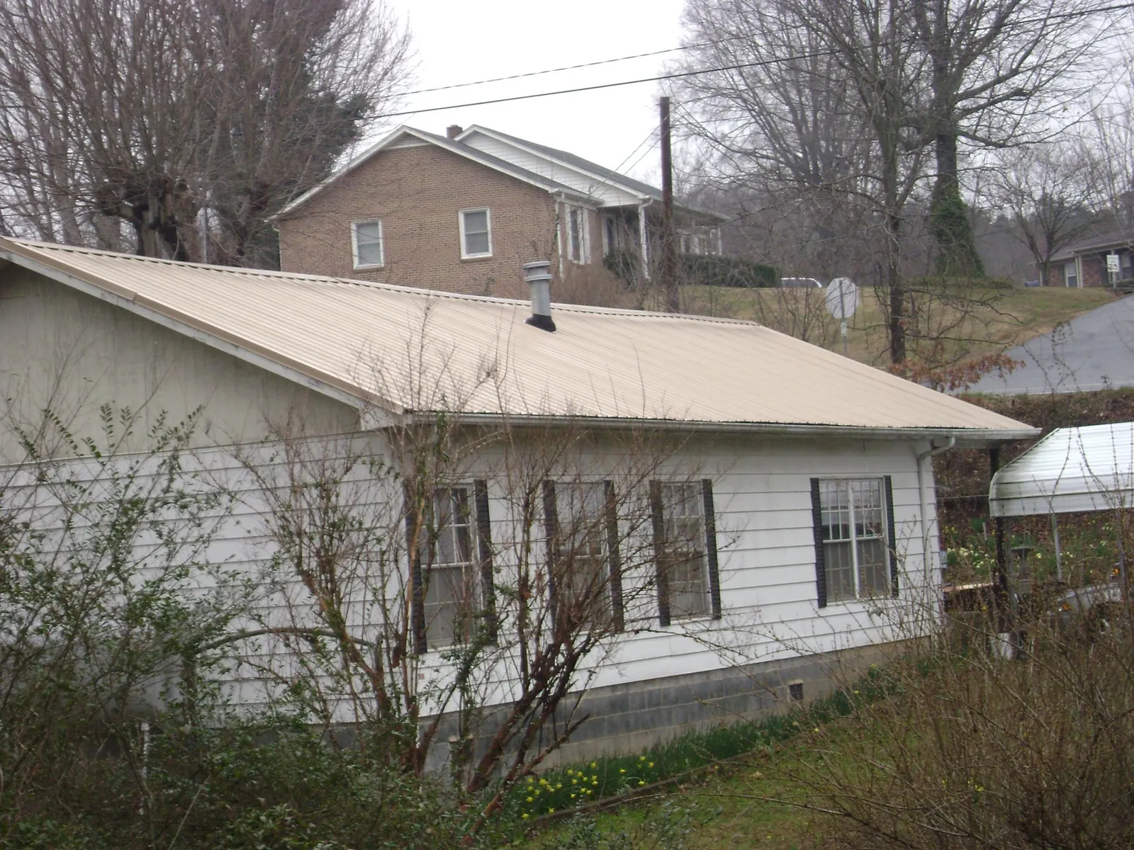 Tan metal roof on a white sided house set into a hillside — Commercial Roofing by Roofing Brothers in Great Falls